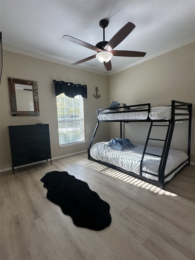 bedroom featuring a textured ceiling, baseboards, a ceiling fan, wood finished floors, and crown molding