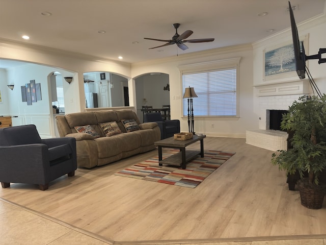 living room with ceiling fan, light hardwood / wood-style floors, ornamental molding, and a fireplace