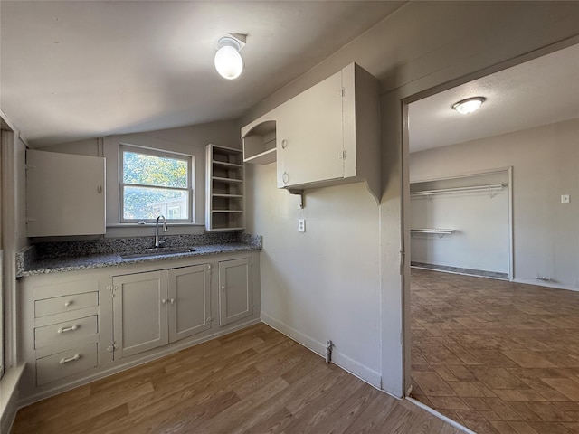 kitchen with vaulted ceiling, white cabinets, sink, and light wood-type flooring