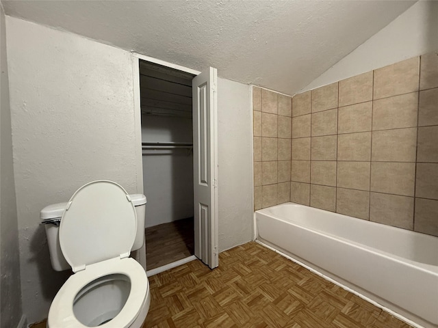 bathroom featuring lofted ceiling, a textured ceiling, a tub to relax in, parquet flooring, and toilet