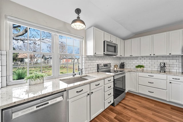 kitchen featuring pendant lighting, lofted ceiling, sink, white cabinetry, and stainless steel appliances