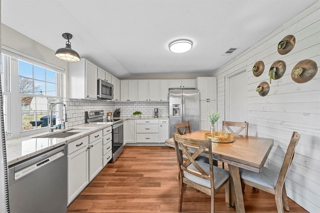 kitchen featuring pendant lighting, white cabinets, sink, light stone countertops, and stainless steel appliances