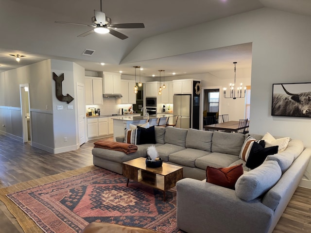 living room with ceiling fan with notable chandelier, dark hardwood / wood-style flooring, and vaulted ceiling