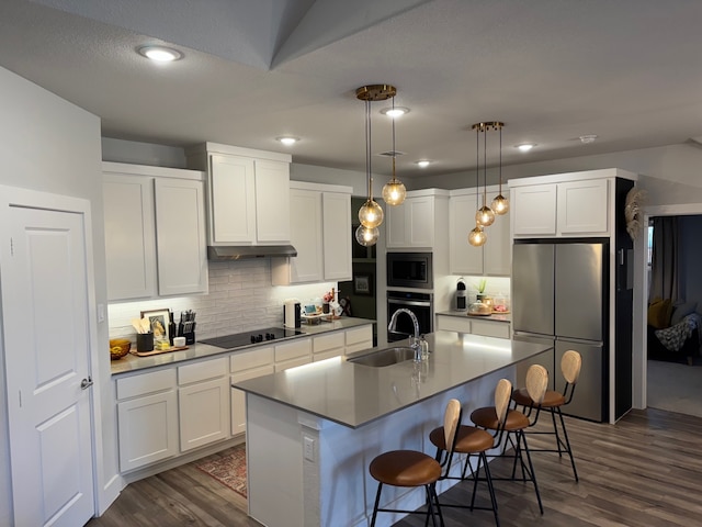 kitchen featuring a center island with sink, sink, hanging light fixtures, white cabinetry, and stainless steel appliances