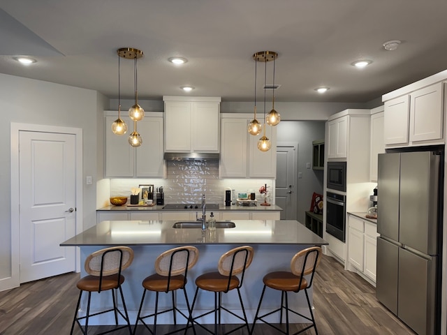 kitchen featuring stainless steel appliances, sink, decorative light fixtures, a center island with sink, and white cabinetry