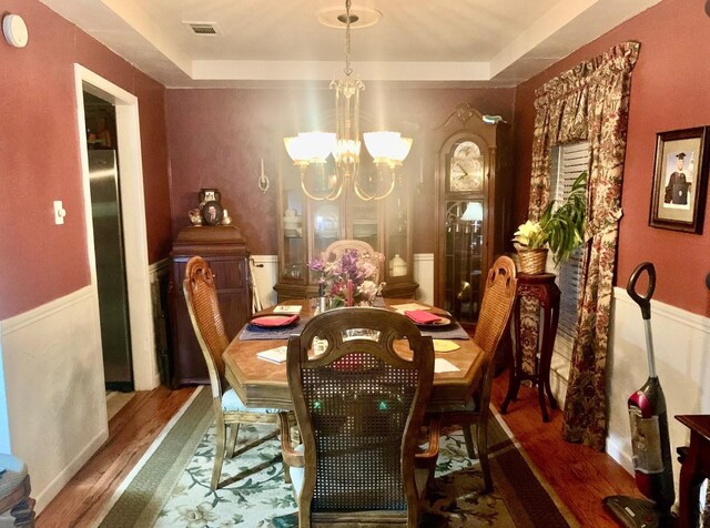 dining space with a tray ceiling, wood-type flooring, and an inviting chandelier