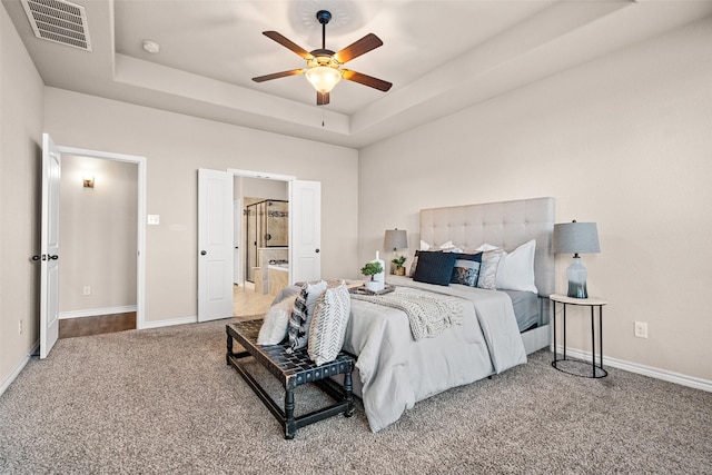 carpeted bedroom with a raised ceiling and ceiling fan