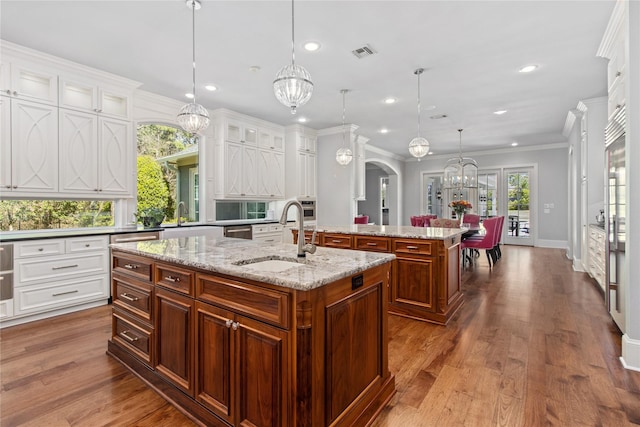 kitchen featuring crown molding, sink, wood-type flooring, pendant lighting, and a center island with sink