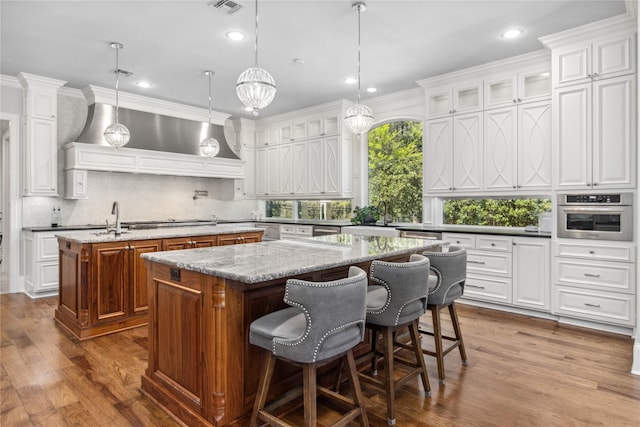 kitchen with hanging light fixtures, an island with sink, decorative backsplash, white cabinets, and appliances with stainless steel finishes