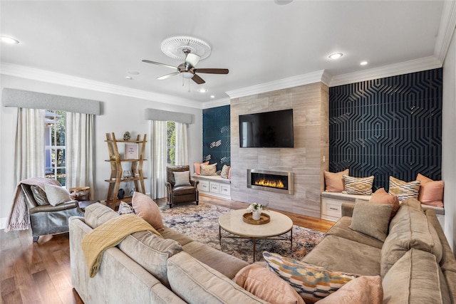 living room with hardwood / wood-style flooring, ceiling fan, ornamental molding, and a fireplace