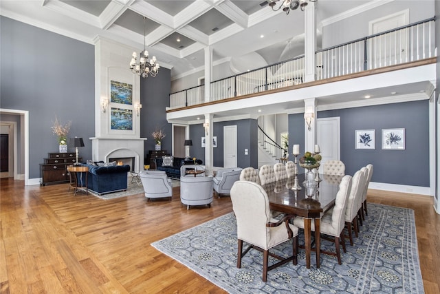 dining area featuring coffered ceiling, a towering ceiling, ornamental molding, beamed ceiling, and wood-type flooring