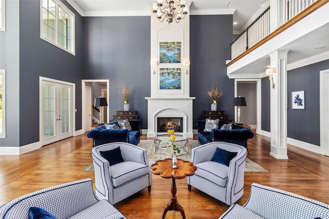 living room featuring a towering ceiling, an inviting chandelier, ornate columns, and ornamental molding