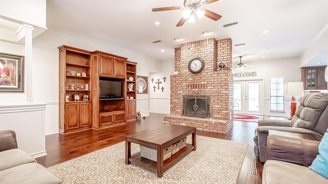 living room featuring dark hardwood / wood-style floors, a brick fireplace, ceiling fan, and ornate columns