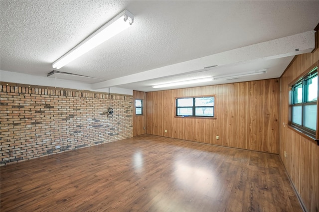 basement featuring wooden walls, hardwood / wood-style floors, brick wall, and a textured ceiling