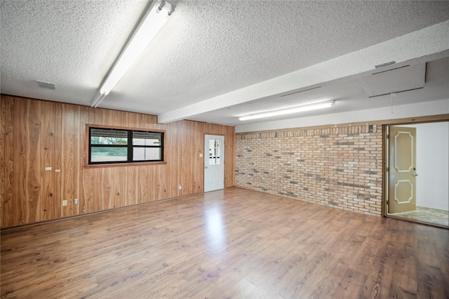 unfurnished room featuring wooden walls, hardwood / wood-style flooring, a textured ceiling, beam ceiling, and brick wall