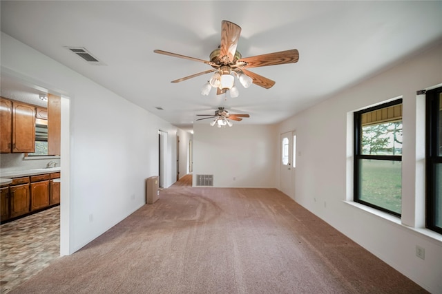 unfurnished living room featuring ceiling fan, sink, and light colored carpet