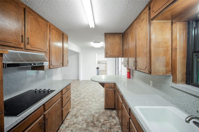 kitchen with kitchen peninsula, black electric cooktop, sink, and tasteful backsplash