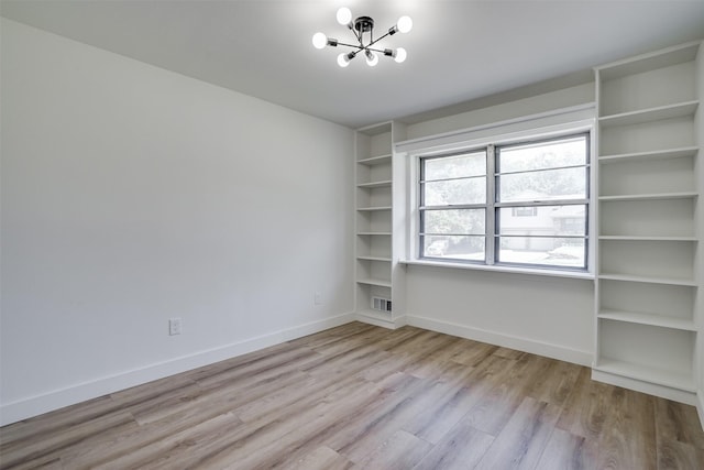 spare room with a chandelier and light wood-type flooring