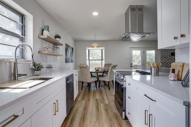 kitchen with white cabinets, wall chimney range hood, hanging light fixtures, appliances with stainless steel finishes, and tasteful backsplash