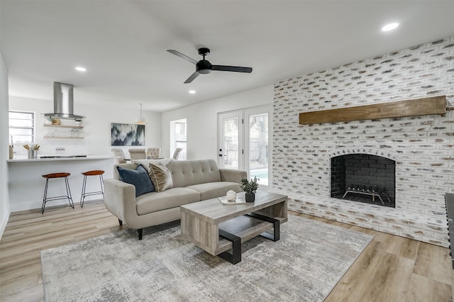 living room with a large fireplace, ceiling fan, and light hardwood / wood-style flooring