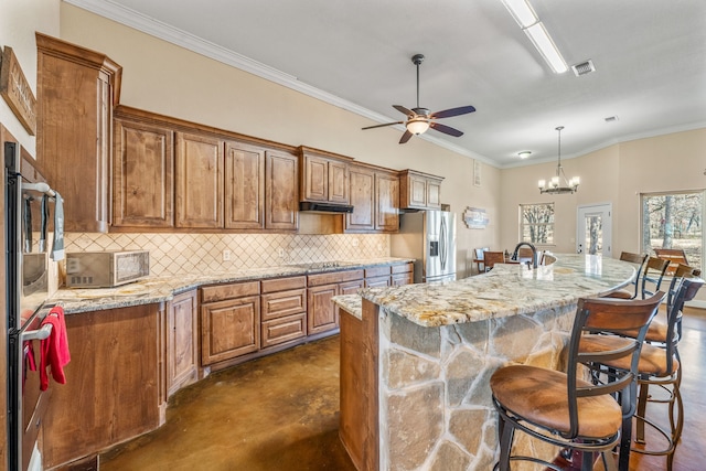 kitchen featuring ceiling fan with notable chandelier, stainless steel fridge with ice dispenser, an island with sink, and tasteful backsplash