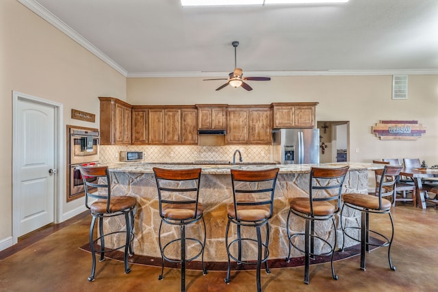 kitchen with decorative backsplash, ornamental molding, a breakfast bar, stainless steel appliances, and an island with sink