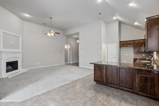 kitchen featuring dark stone countertops, decorative backsplash, ceiling fan, light colored carpet, and dark brown cabinets