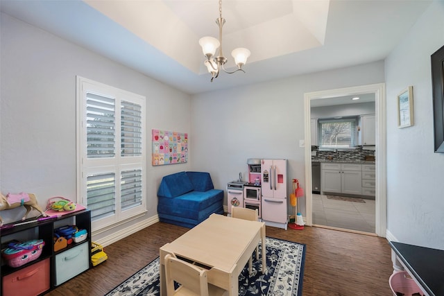 recreation room with dark wood-type flooring, a wealth of natural light, a notable chandelier, and a tray ceiling