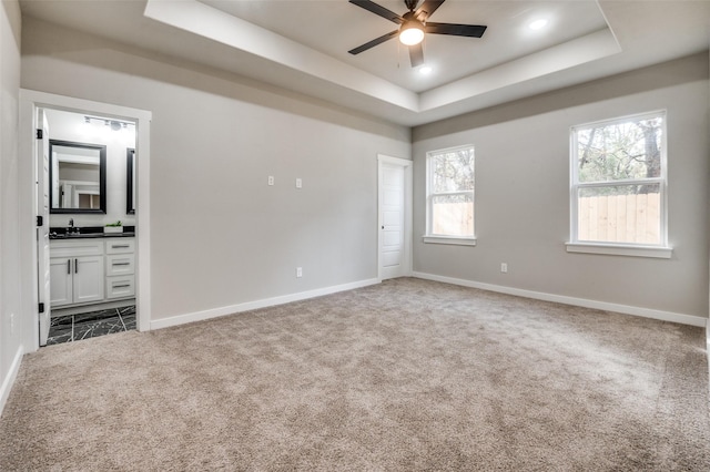 unfurnished room featuring a raised ceiling, ceiling fan, sink, and carpet floors