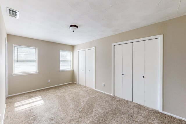 unfurnished bedroom featuring carpet flooring and two closets