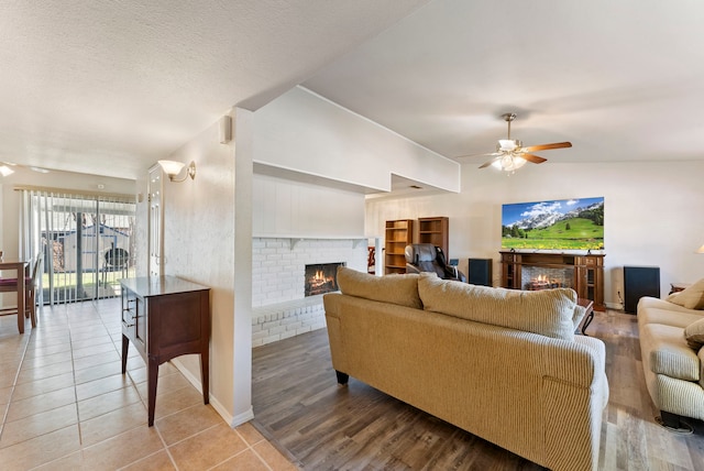 living room featuring ceiling fan, tile patterned flooring, a textured ceiling, lofted ceiling, and a fireplace