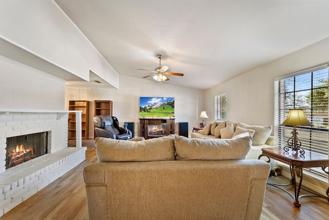 living room featuring ceiling fan, light hardwood / wood-style floors, lofted ceiling, and a brick fireplace