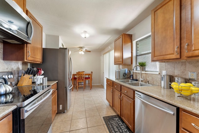 kitchen with light stone countertops, ceiling fan, sink, stainless steel appliances, and light tile patterned flooring