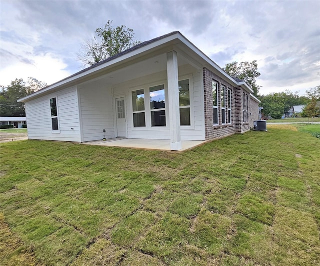 back of property with central AC unit, a patio area, and a lawn