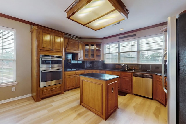 kitchen featuring sink, light wood-type flooring, ornamental molding, appliances with stainless steel finishes, and a kitchen island