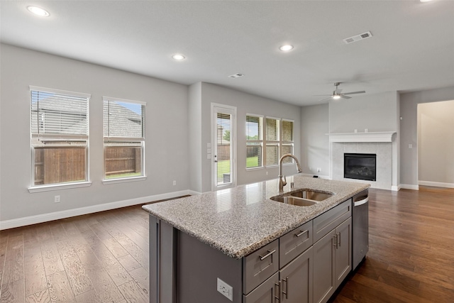 kitchen with light stone countertops, ceiling fan, sink, a tile fireplace, and a center island with sink