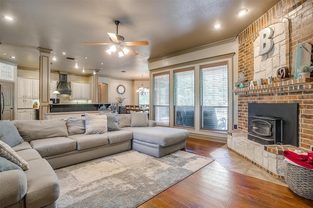 living room with ceiling fan with notable chandelier, light hardwood / wood-style floors, a wood stove, and crown molding