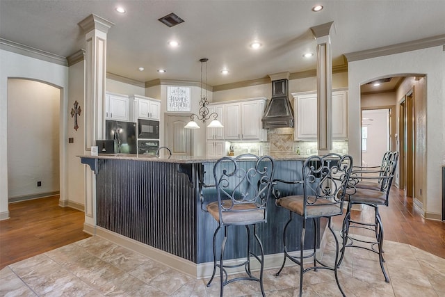 kitchen with light stone countertops, tasteful backsplash, premium range hood, a breakfast bar area, and black appliances