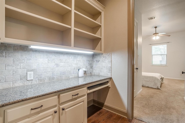 kitchen featuring ceiling fan, dark hardwood / wood-style floors, light stone countertops, built in desk, and tasteful backsplash