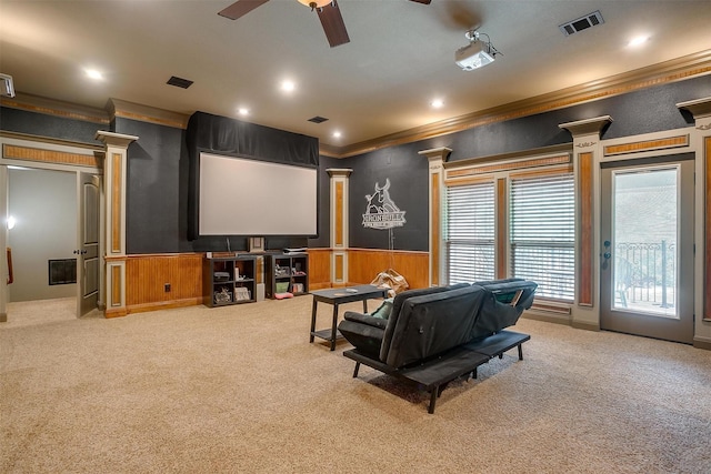 cinema room featuring carpet, ornate columns, ornamental molding, ceiling fan, and wood walls