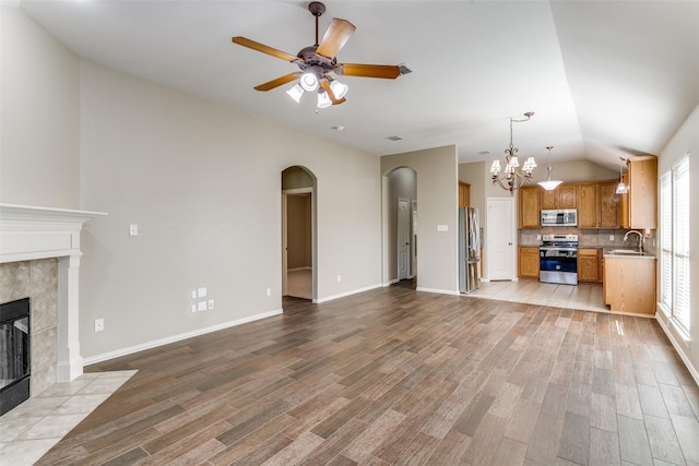 unfurnished living room with ceiling fan with notable chandelier, sink, vaulted ceiling, light wood-type flooring, and a fireplace