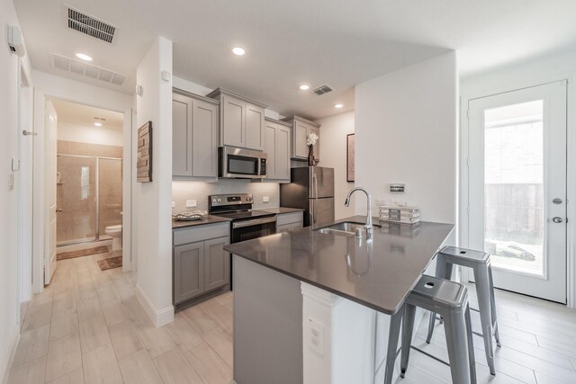 kitchen with kitchen peninsula, appliances with stainless steel finishes, a breakfast bar, sink, and gray cabinets