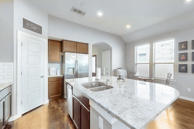 kitchen with sink, vaulted ceiling, an island with sink, appliances with stainless steel finishes, and light stone counters