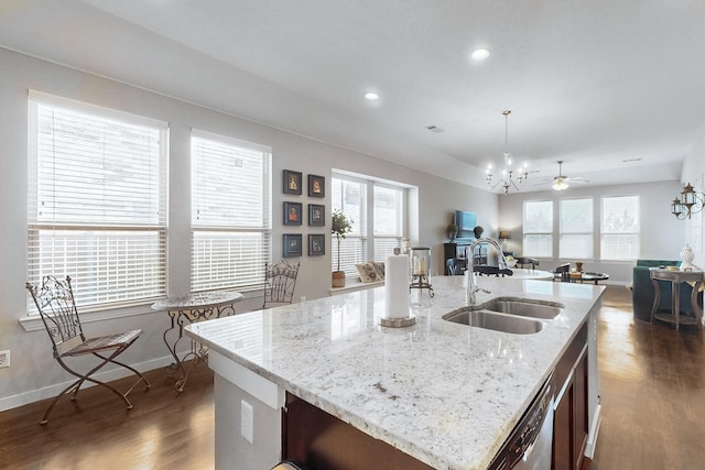 kitchen with sink, decorative light fixtures, dark hardwood / wood-style flooring, light stone countertops, and a kitchen island with sink