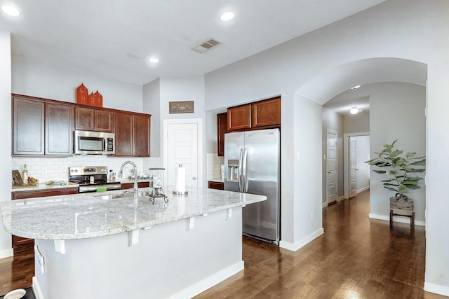 kitchen featuring appliances with stainless steel finishes, dark hardwood / wood-style floors, a breakfast bar, sink, and a kitchen island with sink