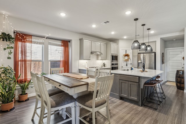 kitchen featuring pendant lighting, stainless steel appliances, gray cabinets, and a center island with sink