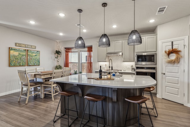 kitchen featuring white cabinetry, hanging light fixtures, appliances with stainless steel finishes, and an island with sink