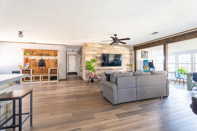 living room featuring ceiling fan, wooden walls, visible vents, and wood finished floors