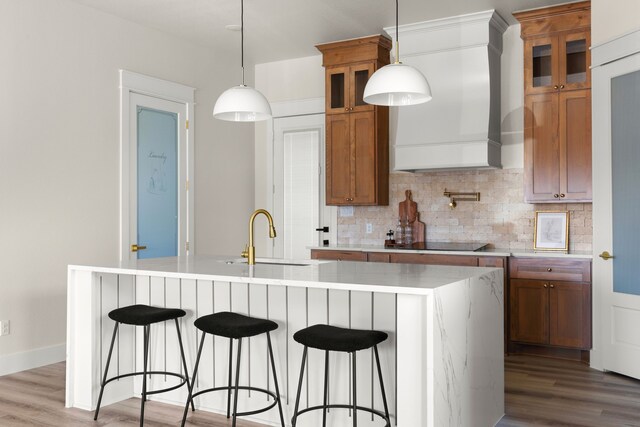 kitchen featuring an island with sink, hanging light fixtures, custom range hood, and hardwood / wood-style flooring