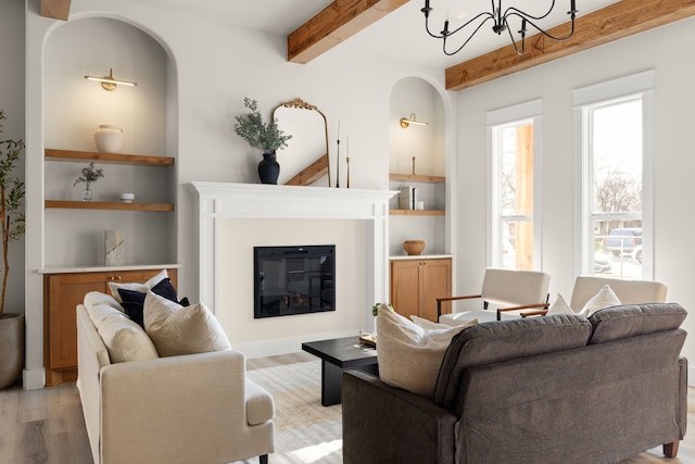 living room with an inviting chandelier, built in features, beam ceiling, and light hardwood / wood-style flooring